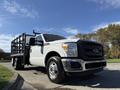 A white 2016 Ford F-350 Super Duty pickup truck with a flatbed and metal sides positioned at an angle, showcasing its front grille and headlights