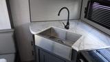 A modern kitchen sink with a sleek stainless steel basin is integrated into a marble countertop featuring a high-arched black faucet