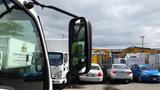 A 2016 Hino 195 truck with a large side mirror reflecting nearby vehicles and equipment