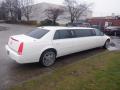 A white 2008 Cadillac Limousine with tinted windows and chrome wheels parked on a wet surface