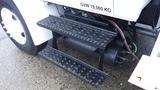 A side view of a black metal step assembly attached to a 2005 International 4300 truck with a visible air tank and braided hoses