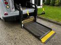 A black and yellow wheelchair lift extended from the back of a 2015 Chevrolet Express van with yellow handles on either side