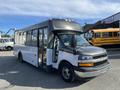 A 2017 Chevrolet Express bus with a white and gray exterior featuring large windows and a front driver's seat visible