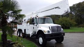 A white 2005 International 7400 bucket truck with an raised boom and an enclosed utility body