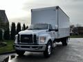 A white 2022 Ford F-750 box truck with a large cargo area and orange roof lights parked on a roadway