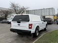 A white 2018 Ford F-150 with a matching cap on the bed parked on a lot with vehicles in the background