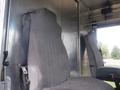 Two grey upholstered seats are positioned inside a vehicle cabin with a metallic interior. The seats have a simple design featuring vertical stitching and a seatbelt on one of them