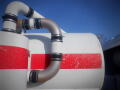 A close-up of a large tank with a red stripe and multiple metal pipes connected to it