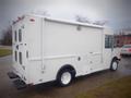 A white 2003 Freightliner MT45 Chassis with a boxy design featuring multiple doors and a rear step for access