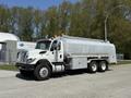 A 2009 International 7500 truck with a silver tanker body and orange safety lights parked on a road