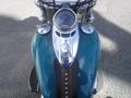 A 2009 Harley-Davidson Flstc with a chrome and teal fuel tank showing a speedometer and ignition switch on top