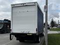 A 2006 Hino 268 box truck with a white rear and blue tarpaulin covering the cargo area parked alongside a street