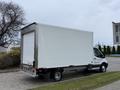 A white 2018 Ford Transit box truck with a flatbed and a rear roll-up door parked at an angle