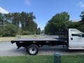 A white 2013 Ford F-450 SD flatbed truck with a black flatbed and side rails is parked on the side of a road