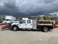 A white 2010 Ford F-550 with a snow plow attachment on the front and a utility bed in the back parked on a lot
