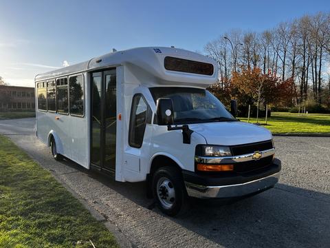 A white 2017 Chevrolet Express with a large passenger door and signage area on the front, featuring chrome accents and a boxy design suitable for group transportation