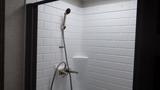 A shower stall with white subway tile featuring a handheld showerhead and a faucet assembly mounted on the wall