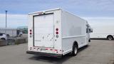 A white 2011 Ford Econoline with a boxy cargo area and a rear roll-up door parked in a lot