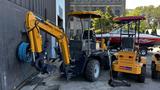 A yellow 2024 AGT BH50G backhoe loader with an extended arm and bucket attached, positioned next to a wall and other equipment