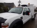 A 2009 Ford F-450 Super Duty truck with a white exterior and a flatbed, equipped with a tool compartment and amber rooftop lights