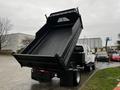 A white 2005 GMC C5 Duramax dump truck with its bed raised, displaying an empty black cargo area