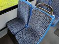 Two blue and patterned bus seats closely arranged next to each other with a metal handrail on the back of one seat