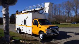 A yellow 2015 Ford Econoline van with a white body and a raised aerial platform attached on top