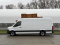 A 2019 Mercedes-Benz Sprinter van with a white exterior and black lower trim parked beside wooden crates on its roof