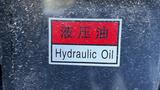 A label displaying the words Hydraulic Oil and additional text in another language on a dark surface