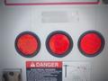 A close-up view of three round red lights on a 2006 Freightliner FS65 with a warning sign below indicating electrical hazards