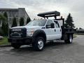 A 2015 Ford F-550 with a flatbed truck design featuring a black canopy and orange cargo lights on the roof