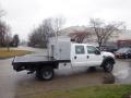 A white 2009 Ford F-450 SD with a flatbed and a toolbox mounted on the side parked on a road