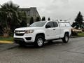 A white 2019 Chevrolet Colorado pickup truck parked on a street with a camper shell on the bed