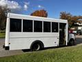 A white 2015 Chevrolet Express bus with large windows and a door on the side parked on grass near a road