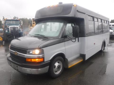 A 2016 Chevrolet Express bus with a white and gray exterior features a large front windshield and several side windows for passenger visibility