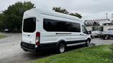 A white 2017 Ford Transit van parked on a street showcasing its side profile and large rear windows