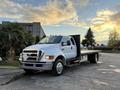 A white 2006 Ford F-650 truck with a flatbed and chrome grille parked on a concrete surface