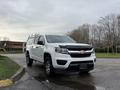 A white 2018 Chevrolet Colorado with a black front grille and an extended cab featuring a ladder rack on top