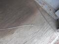 A thin metal cable with a small end piece resting on a wooden floor surface