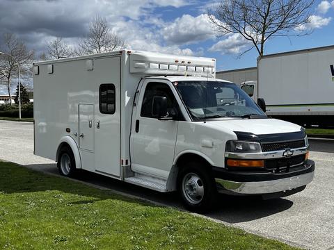 A white 2013 Chevrolet Express van with a boxy shape and side steps parked on a lot
