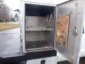 An open storage compartment of a 2009 Ford F-450 SD featuring hooks on the interior wall and a wooden panel with tools attached