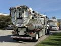 A 2013 International 7400 truck equipped with a large, cylindrical vacuum tank and multiple hoses mounted on the rear for industrial cleaning purposes