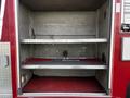 Interior view of a red fire truck compartment with metal shelves and a red rubber mat on the floor