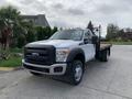 A 2012 Ford F-550 truck with a flatbed and black grille is parked with its headlights on