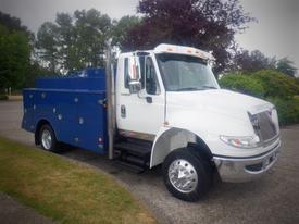 A white 2012 International DuraStar 4300 truck with a blue utility body and chrome wheels parked on a driveway