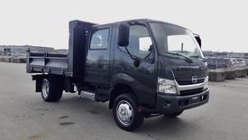 A dark green 2015 Hino 195 Crew Cab truck with a flatbed and a cab for crew seating visible in the foreground