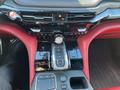 Interior view of a 2023 Acura MDX featuring a sleek center console with a gear shift dial buttons and a touchpad surrounded by a glossy black finish and red leather accents