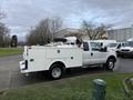 A 2013 Ford F-350 SD truck with a white utility body and a mounted equipment on top parked on a street