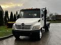 A white 2006 Hino 155 truck with a flatbed and a black grille featuring a large silver logo on the front