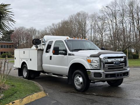 A white 2013 Ford F-350 SD truck with a service body and tools in the bed parked at an angle